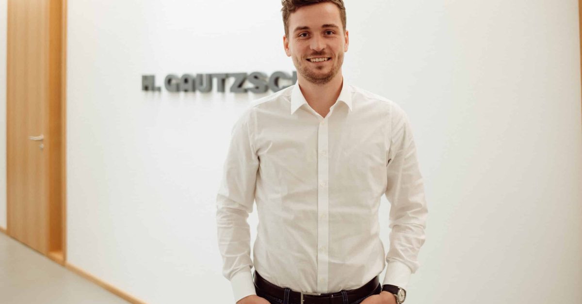 Mann mit weißem Hemd steht in einem hellen Flur mit H. Gautzsch Schriftzug im Hintergrund