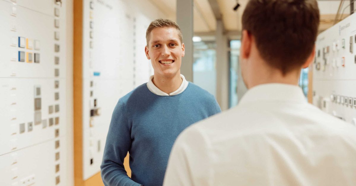 Lächelnder junger Mann in blauem Pullover spricht mit einem anderen Mann in einem modernen Büro